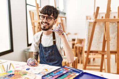 Resim stüdyosunda sakallı, gülümseyen, el ve parmaklarıyla telefonla konuşan İspanyol bir adam. iletişim kavramları. 