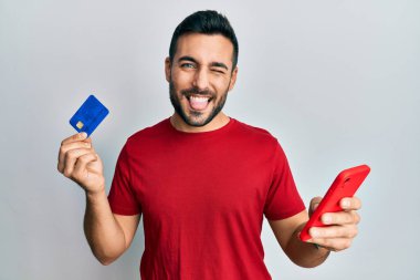 Akıllı telefon ve kredi kartı tutan İspanyol genç adam komik bir ifadeyle dilini dışarı çıkarıyor.. 
