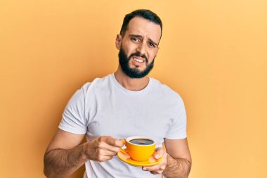 Sakallı genç adam bir fincan kahve içiyor habersiz ve kafası karışmış bir ifade. şüphe kavramı. 