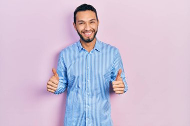 Sakallı, günlük mavi tişörtlü İspanyol bir adam. Başarı işareti yapıyor. Elleriyle olumlu jest yapıyor. Neşeli ifade ve kazanan jest. 