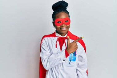 Genç Afro-Amerikan kadın doktor üniforması giyiyor ve süper kahraman kostümü giyiyor. Gülümsüyor, gülümsüyor. 