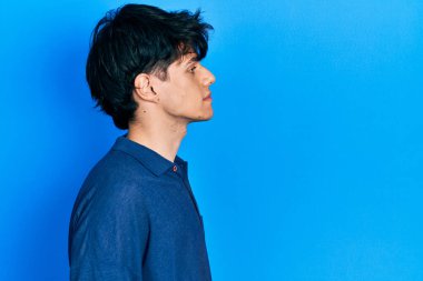 Yakışıklı hippi genç adam mavi arka planda mahsur kalmış, yan tarafa bakıyor, rahat poz veriyor, kendine güvenen bir gülümsemesi var.. 