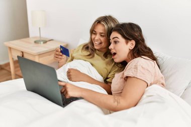 Yatak odasında kredi kartı ve laptop kullanan genç bir çift.