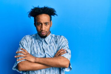 Sakallı, sıradan giyinen, kuşkucu ve gergin, yüzünde çapraz kollu tasvip etmeyen genç Afro-Amerikan bir adam. negatif kişi. 