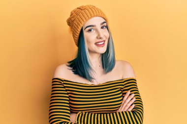 Yün şapka takan, kollarını kavuşturup kameraya gülümseyen genç, modern bir kız. pozitif kişi. 