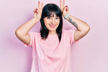 Genç İspanyol kadın gündelik kıyafetler giyiyor komik ve çılgın poz veriyor parmakları tavşan kulağı gibi, neşeli gülümsüyor 