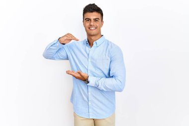 İzole edilmiş arka planda duran iş gömleği giyen genç İspanyol adam. Ellerinde büyük ve büyük bir işaret, ölçü sembolü var. Kameraya bakıp gülümsüyor. ölçüm kavramı. 