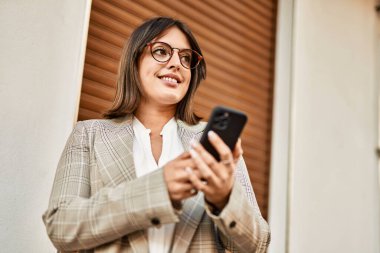 Genç İspanyol iş kadını şehirde akıllı telefon kullanarak mutlu gülümsüyor..