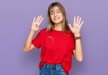 Gündelik kırmızı tişört giyen genç beyaz kız dokuz numarayı gösteriyor ve gülümsüyor. Kendinden emin ve mutlu.. 