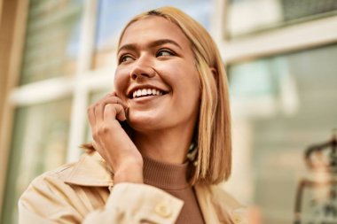 Genç sarışın kız gülümsüyor. Şehirdeki akıllı telefondan konuşuyor..