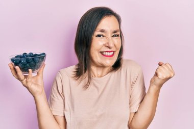 Orta yaşlı İspanyol kadın elinde yaban mersini tutarak gururla bağırıyor zaferi ve başarıyı kutluyor. 