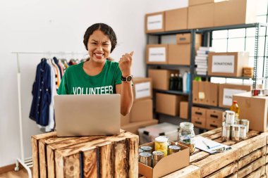 Güzel İspanyol kadın gönüllü tişört giyiyor dizüstü bilgisayarla çalışıyor gururla bağırıyor, zaferi kutluyor ve başarıyı kollarını kaldırarak kutluyor. 