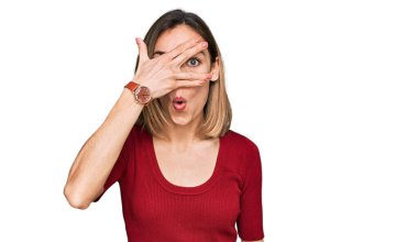 Sıradan kıyafetler giyen genç sarışın kız şok içinde yüzünü ve gözlerini kapayarak utanmış bir ifadeyle parmaklarının arasından bakıyor.. 