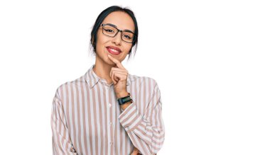 Gündelik kıyafetler ve gözlük takan genç İspanyol kız kameraya kendinden emin bir şekilde bakıyor kollarını kavuşturup, çenesini kaldırarak gülümsüyor. Olumlu düşünmek. 