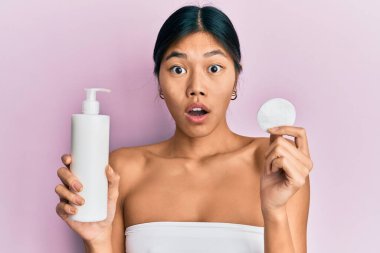 Genç Çinli kadın duş havlusu kullanıyor. Temiz losyon kullanıyor. Şaşırmış ve şaşırmış bir ifade, korku ve heyecanlı bir yüz.. 