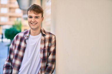 Genç beyaz adam gülümseyerek şehirde mutlu mesut duruyor..