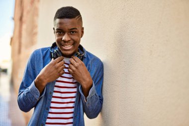Genç Afrikalı Amerikalı adam şehirde kulaklık takarak mutlu bir şekilde gülümsüyor..