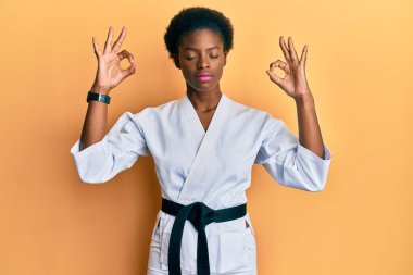 Karate kimonosu ve siyah kuşak giyen, gözleri kapalı gülümseyen, meditasyon yapan, parmaklarıyla meditasyon yapan Afrikalı genç bir Amerikalı kız. yoga konsepti. 