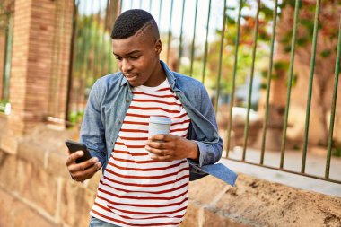 Genç Afrikalı Amerikalı adam akıllı telefon kullanıyor. Şehirde kahve içiyor..