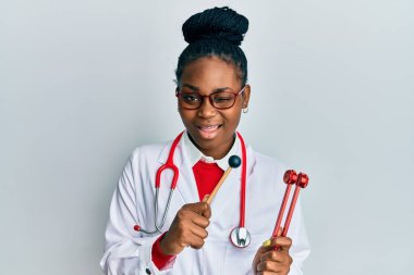 Genç Afro-Amerikan kadın doktor üniforması giymiş elinde çatal tutarak kameraya seksi bir ifadeyle bakıyor, neşeli ve mutlu bir yüzle.. 