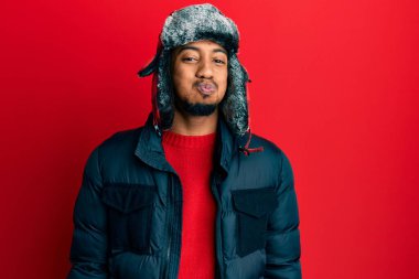 Sakallı, kışlık şapkalı ve paltolu komik yüzlü Afro-Amerikalı genç bir adam. Havayla şişmiş ağız, çılgın bir ifade.. 