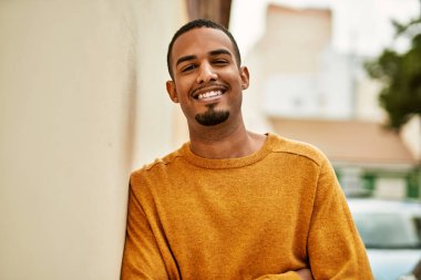 Genç Afrikalı Amerikalı adam gülümseyerek şehirde mutlu mesut duruyor..
