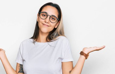 Gündelik beyaz tişört giyen, elleri ve kolları havada, kafası karışmış genç İspanyol kadın. şüphe kavramı. 