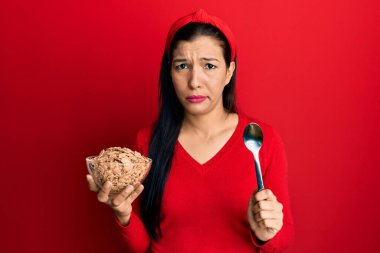 Genç Latin bir kadın elinde mısır gevreği ve kaşık tutarken şüpheci ve gergin, sorun yüzünden somurtuyor. negatif kişi. 