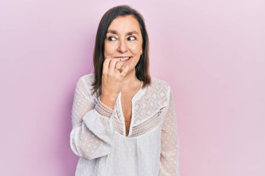 Orta yaşlı İspanyol kadın gündelik kıyafetler giyiyor. Stresli ve gergin görünüyor. Elleri ağızdan tırnak yiyor. anksiyete. 