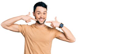 Sakallı, sıradan tişörtlü, neşeli gülümseyen, parmaklarıyla ve ağzıyla işaret eden İspanyol bir adam. diş sağlığı kavramı. 