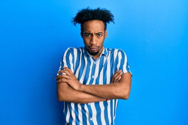 Sakallı, sıradan çizgili tişörtlü, kuşkucu ve gergin, yüzünde çapraz kollu tasvip etmeyen bir ifade olan Afrikalı genç bir Amerikalı. negatif kişi. 