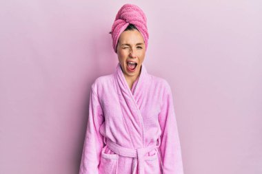 Duş başlığı ve bornoz takan genç sarışın kadın kameraya seksi bir ifadeyle bakıyor, neşeli ve mutlu bir yüzle.. 