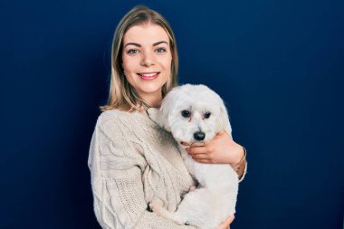 Güzel beyaz kadın sevimli köpeğe sarılıyor pozitif ve mutlu görünüyor ve gülümsüyor kendine güvenen bir gülümsemeyle dişlerini gösteriyor. 