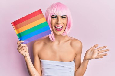 Ellerinde gökkuşağı lgbtq bayrağı olan genç adam başarıyı mutlu bir gülümsemeyle ve kazanan yüz ifadesiyle kutluyor. 