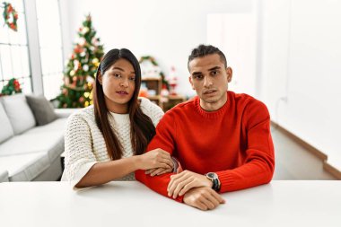 Genç Latin çift Noel ağacının yanında masada oturuyor. Uykulu ve yorgun görünüyorlar. Yorgunluktan ve akşamdan kalmalıktan bitkinler.. 