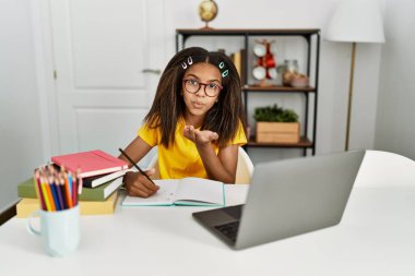 Genç Afro-Amerikan kız evde ödevini yapıyor kameraya bakıyor ve havadan öpücükler savuruyor. Güzel ve seksi. aşk ifadesi. 