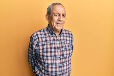 Gri saçlı, sıradan gömlekli yakışıklı bir adam yüzünde gülümsemeyle yan yana bakıyor, doğal bir ifade. Kendinden emin gülen. 