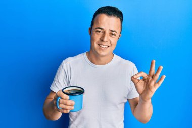 Yakışıklı genç adam bir fincan kahve içiyor parmaklarıyla imza atıyor, gülümsüyor ve mükemmel bir sembol. 