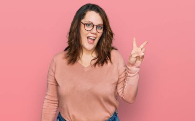 Gündelik kıyafetler ve gözlük takan, kameraya gülümseyen ve parmaklarıyla zafer işareti yapan genç ve cüsseli bir kadın. İki numara.. 