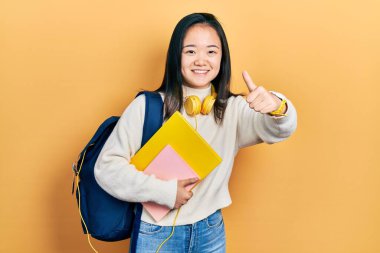 Öğrenci sırt çantası tutan Çinli genç bir kız ve el hareketlerini onaylayan kitaplar, gülümseme ve başarı için mutlu. kazanan jest. 
