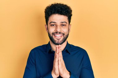 Sakallı, sıradan gömlekli genç bir Arap ellerini birleştirip af diliyor kendinden emin bir şekilde gülümsüyor.. 