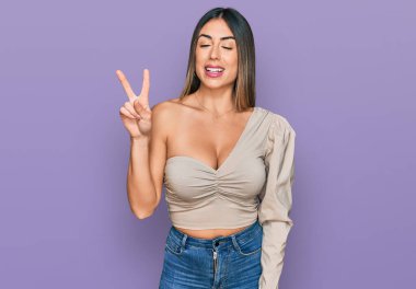 Genç İspanyol kadın gündelik giysiler giyiyor. İki numarayı gösterip işaret ediyor. Kendinden emin ve mutlu bir şekilde gülümsüyor.. 