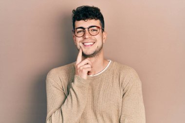 Gündelik giysiler ve gözlük takan genç İspanyol adam kameraya kendinden emin bir şekilde bakıyor kollarını kavuşturup, çenesini kaldırarak gülümsüyor. Olumlu düşünmek. 