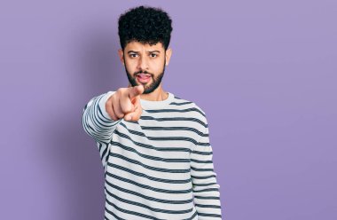 Sakallı, sıradan çizgili süveter giyen genç Arap adam kameraya kızgın ve sinirli bir şekilde bakıyor. 