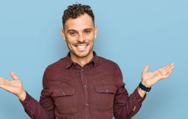 Gündelik kıyafetler giyen genç İspanyol adam gülümseyerek iki elini de açık tutuyor, sunuyor ve reklam karşılaştırması yapıyor ve dengeyi sağlıyor. 