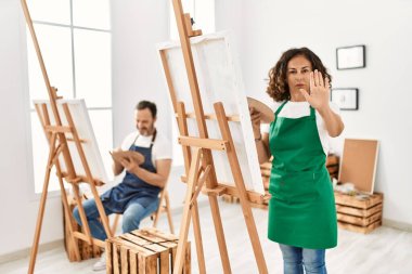 İspanyol orta yaşlı kadın ve sanat stüdyosunda eli açık olgun bir adam ciddi ve kendinden emin bir ifadeyle dur işareti yapıyor. 