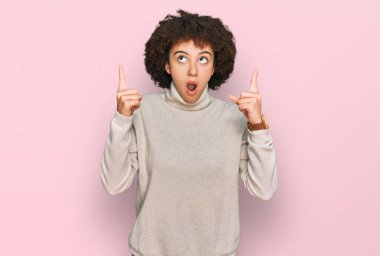 Kışın yün kazak giyen İspanyol genç kız şaşırmış ve şaşırmış bir şekilde yukarı bakıyor ve parmaklarıyla işaret ediyor ve kollarını kaldırıyordu.. 