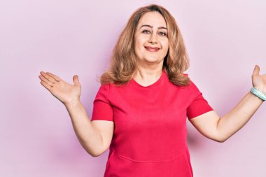 Orta yaşlı beyaz kadın, gündelik kıyafetler giyiyor, elleri ve kolları havada, kafası karışmış bir ifade takınıyor. şüphe kavramı. 