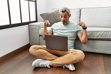 Orta yaşlı İspanyol bir adam oturma odasında dizüstü bilgisayar kullanıyor. Parmaklarını göstererek reklamını yapıyor, şaşırmış yüzünü gösteriyor ve ağzını açıyor. 