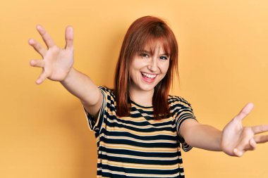 Kızıl saçlı, sıradan çizgili tişört giyen genç bir kadın kameraya sarılıp gülümseyerek bakıyor. Mutluluğu kucaklayan neşeli bir ifade.. 